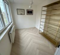 Szoba egy kétszobás lakásban polccal, fa dekorációjú padlóval és ablakkal.