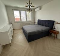 Hálószoba ággyal, fehér komóddal, fa hatású padlóval és függőlámpával.