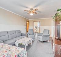 Nappali egy négy szobás lakásban szürke kanapéval, asztallal és mennyezeti ventilátorral.