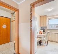 Egy 4 szobás lakás belső tere fa mintázatú padlóval és világos konyhával.