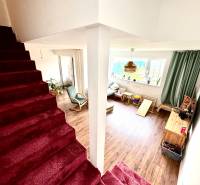 Családi ház belső tere lépcsőházzal és nappalival, fa mintázatú padlóval.