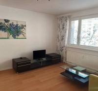 Nappali fa mintázatú padlóval, háromszobás lakásban, amely magában foglalja a televíziót és az asztalt.