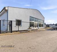 Üzlethelyiség Párkányban szürke homlokzattal, parkolóval és előtetővel.