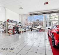 Autószerviz üzlethelyiség üveggel és kiállított autóval a burkolaton, alkatrészek a falakon.