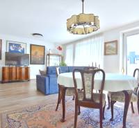 Nappali étkezőasztallal, kanapéval és fa dekorációjú padlóval egy háromszobás lakásban.