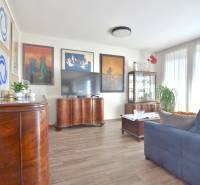 Nappali sötét bútorokkal, fa dekoros padlóval és dekoratív képekkel egy háromszobás lakásban.