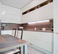 Konyha egy háromszobás lakásban fényes szekrényekkel és fa dekorációjú falakkal.