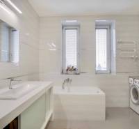 Fürdőszoba egy háromszobás lakásban zuhanyzóval, mosógéppel és redőnyös ablakokkal.