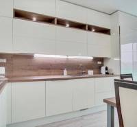 Konyha egy háromszobás lakásban fehér bútorokkal és fa mintájú padlóval.