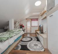 Családi ház tetőtéri szobája ággyal, TV-vel, dekorációkkal és fa mintázatú padlóval.