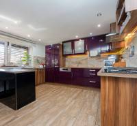 Családi ház konyhája fényes lila szekrényekkel és fa dekoros padlóval.