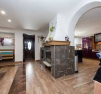 Családi ház belső tere kandallóval, fa dekor padlóval, konyha, bejárati ajtó.