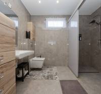 Családi ház fürdőszobája csempével és zuhanyzóval, fa dekorral ellátott szekrényekkel.