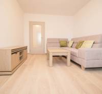 Nappali egy háromszobás lakásban kanapéval és fa mintázatú padlóval.