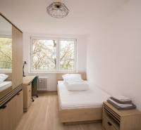 Szoba egy háromszobás lakásban ággyal, asztallal és fa dekorációjú padlóval.