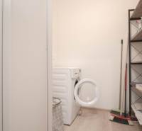 Mosókonyha egy háromszobás lakásban mosógéppel, polccal és tisztítószerekkel.