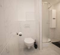 Fürdőszoba zuhanyzóval, WC-vel és fehér csempékkel egy háromszobás lakásban.