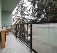 Erkély egy 3 szobás lakásban bútorokkal és korláttal, kilátással a zöldre.