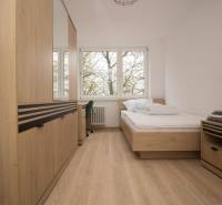 Világos hálószoba egy háromszobás lakásban, fa dekorációs padlóval és nagy ablakokkal.