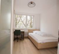 Egyágyas hálószoba ággyal, íróasztallal és fa dekorációjú padlóval egy háromszobás lakásban.