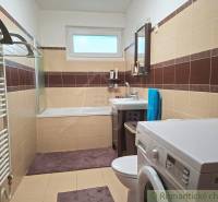 Családi ház fürdőszobája káddal, mosógéppel és barna-bézs csempével.