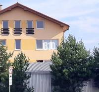 Sárga ház ferde tetővel és ablakokkal a fák mögött, közel az irodai vonalakhoz.