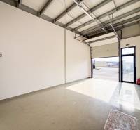 Kereskedelmi helyiségek nagy garázskapuval és szürke padlóval, világítással.