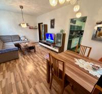 Nappali egy háromszobás lakásban fa dekor padlóval, kanapéval és televízióval.