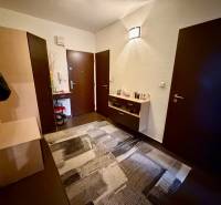 Előszoba sötét ajtókkal, komóddal és fa dekorációs padlóval egy háromszobás lakásban.