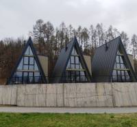 Háromszögletű tetővel rendelkező házak az Evy utcában, Holčíkovce településen, természet és erdő által körülvéve.