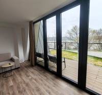 Ház belső tere kanapéval, fa dekorációjú padlóval, nagy ablakokkal, kilátással a teraszra.