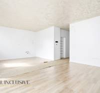 Tágas szoba fehér falakkal és fa dekorációjú padlóval egy háromszobás lakásban.