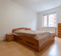 Világos falú szoba, franciaággyal és fa mintázatú padlóval egy kétszobás lakásban.