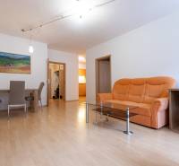 Nappali egy kétszobás lakásban narancssárga kanapéval és fa mintázatú padlóval.