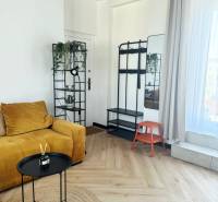 A háromszobás lakásban található egy mustársárga kanapé, egy állvány, egy tükör és fa dekorációjú padló.