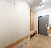 Bejárati folyosó fa mintázatú padlóval egy kétszobás lakásban fehér szekrényekkel.