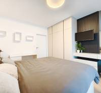 Hálószoba egy kétszobás lakásban ággyal, ruhásszekrénnyel és falra szerelt televízióval.