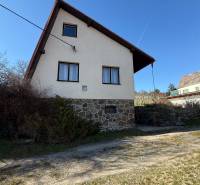 Kunyhó Aranyosmaróton kőalappal és ferde tetővel a kék ég alatt.