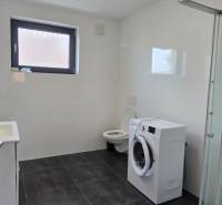 Fürdőszoba egy háromszobás lakásban zuhanyzóval, mosógéppel és fekete csempével.