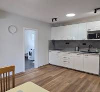 Konyha fehér szekrényekkel és készülékekkel egy háromszobás lakásban, fa dekor padlóval.