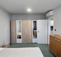 Szoba egy háromszobás lakásban ággyal, szekrénnyel, légkondicionálóval és fa dekorációjú bútorokkal.