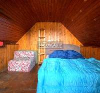 Padlásszoba fa burkolattal, ággyal és ülőgarnitúrával a házikóban.