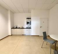 Irodai helyiségek konyhával, fehér szekrényekkel és szürke székekkel.