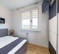 Hálószoba ággyal és televízióval, fa dekorációjú padlóval egy háromszobás lakásban.