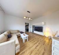 Nappali fa mintás padlóval egy háromszobás lakásban, világos kanapéval és TV szekrénnyel.