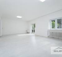 Tágas nappali egy 4 szobás lakásban fehér padlóval és nagy ablakokkal.