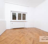 Szoba egy 4 szobás lakásban fehér falakkal és fa dekoros padlóval.