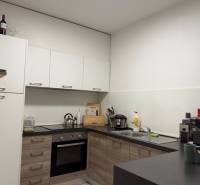 Konyha egy kétszobás lakásban, fa hatású padlóval és fehér szekrényekkel.