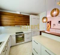 Családi ház konyhája konyhabútorral, függőlámpákkal és beépített készülékekkel.