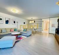 Nappali egy családi házban kanapéval, dekorációkkal és fa mintázatú padlóval.